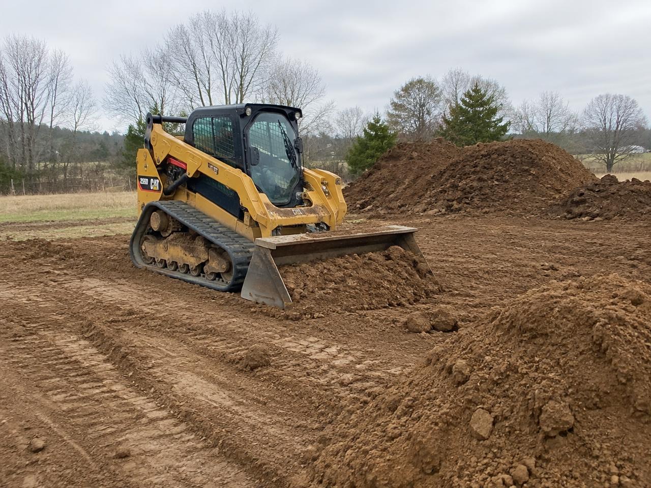 Track loader moving piles of fresh soil on a rural building site