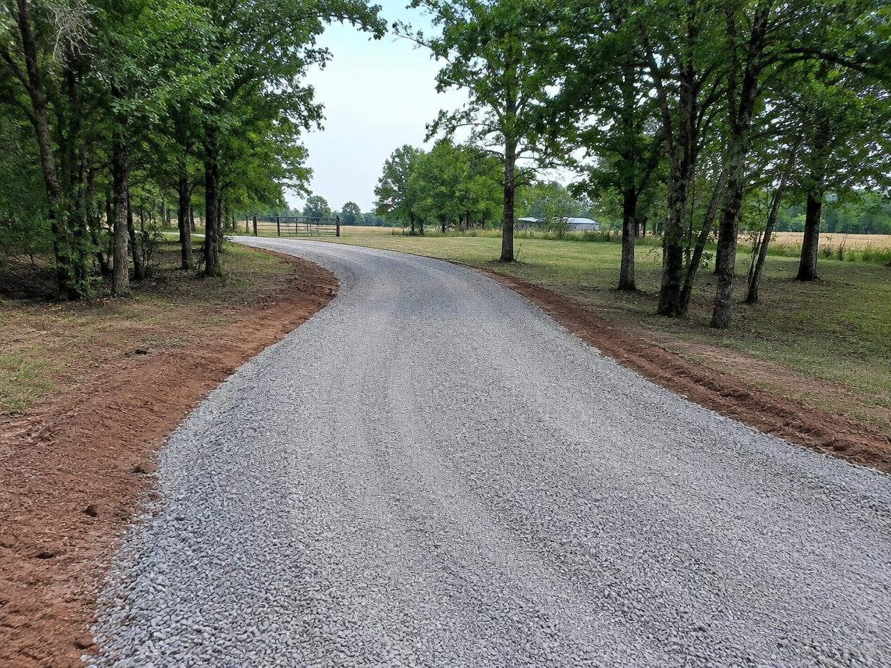 Freshly graded gravel driveway winding through trees on a rural Oklahoma property